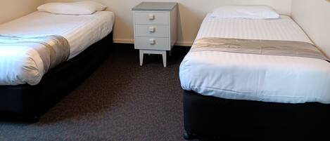 A hotel room with two beds, a small bedside table, a wall-mounted painting, and a carpeted floor.