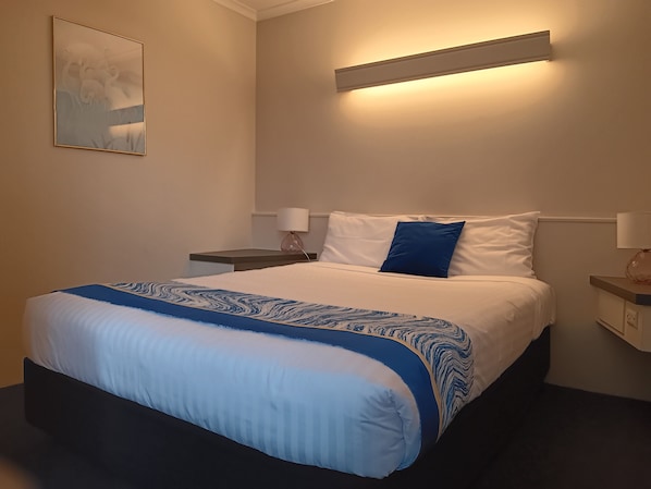 Una habitación de hotel con cama, mesitas de noche, una lámpara de pared y un cuadro.