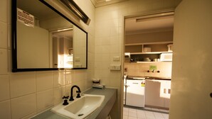 A bathroom with a sink, mirror, and a door leading to a kitchen area. - Parklane Motel (Launceston)
