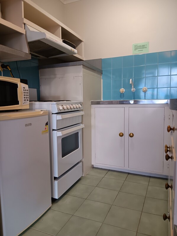A kitchen with a white refrigerator, oven, and microwave. There is a sink with a faucet and a cabinet with a door. - Parklane Motel (Launceston)