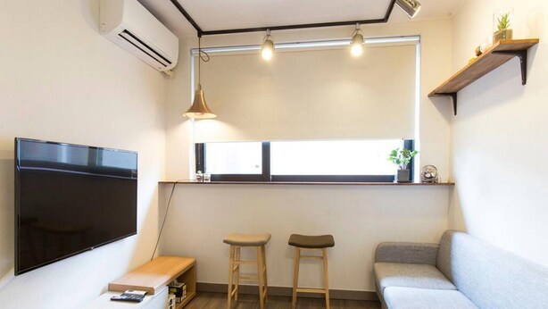 A modern living room with a flat-screen TV, a wooden bench, a grey sofa, and a window with a view. - Hongdae Sopoong the Urban (Seoul)