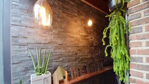 A reception area with a stone wall, wooden bench, hanging plants, and pendant lighting. - Hongdae Sopoong the Urban (Seoul)