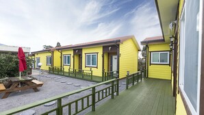 Un bâtiment jaune avec une terrasse verte, des sièges à l’extérieur et un parasol rouge.