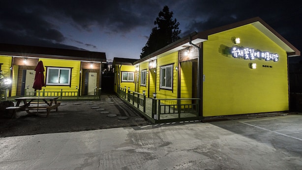 Un bâtiment jaune avec une enseigne dans une langue étrangère, une table de pique-nique et une rambarde.