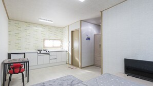Une pièce compacte comprenant un coin cuisine, une télévision, un lit et une petite table avec une chaise.