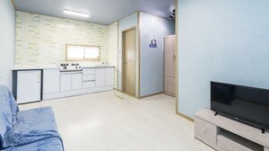 Un espace de vie compact comprenant un coin cuisine, un téléviseur et une porte donnant sur une autre pièce.