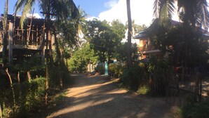 A dirt road flanked by palm trees and vegetation, leading to a building with a blue roof. - WEStay @ Chillax House - Ngapali - Hostel (Ngapali)