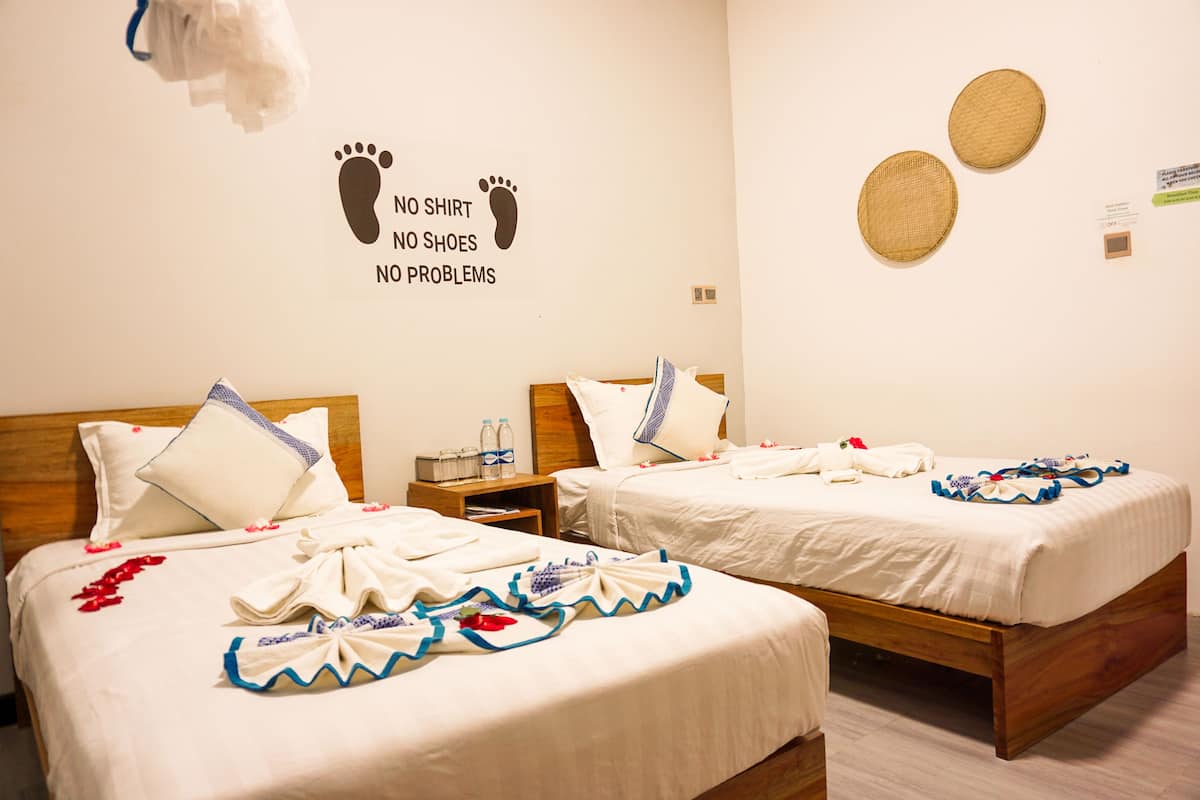 Ett hotellrum med två sängar, där varje säng har ett prydligt påslakan och kuddar. Det finns två korgar som är fästa på väggen och en väggdekor med ett fotavtryck och text.