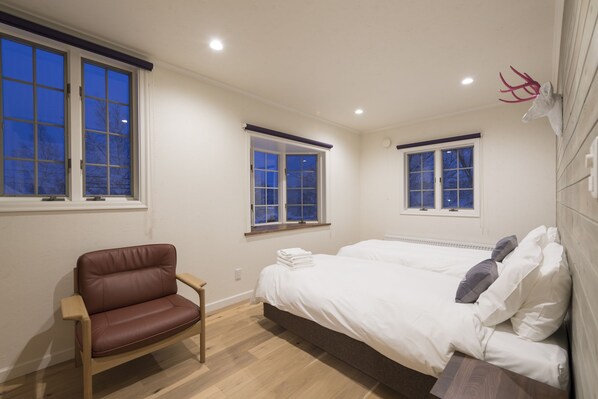 Un dormitorio con una cama grande, dos ventanas, un sillón de cuero marrón y una cabeza de venado montada en la pared.