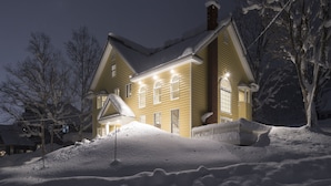 Lumipeitteinen talo, jossa on savupiippu, ikkunat ja lumipeitteinen katto.