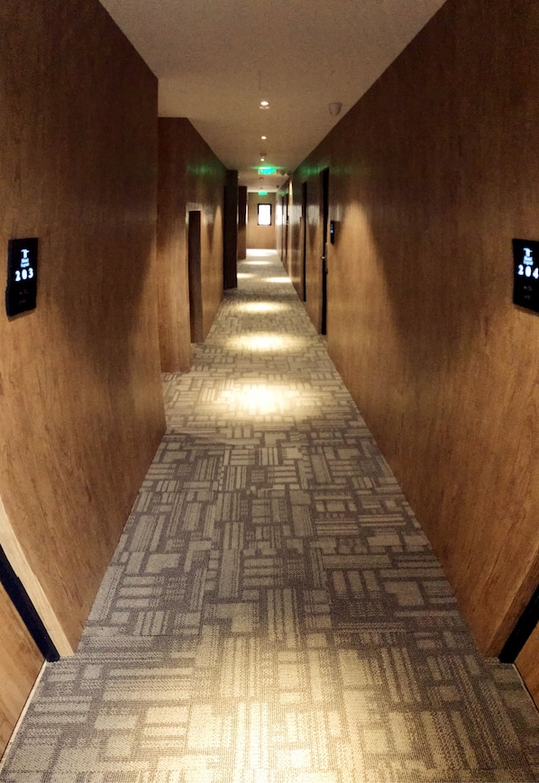 A hotel hallway with patterned carpet, wooden walls, and illuminated exit signs.