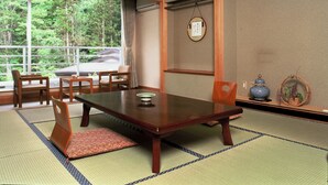 Una habitación japonesa tradicional con suelo de tatami, una mesa baja y vistas a un bosque a través de amplios ventanales.