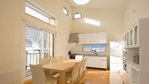 Uma cozinha moderna com armários brancos, uma mesa de jantar com cadeiras e vista para o exterior.