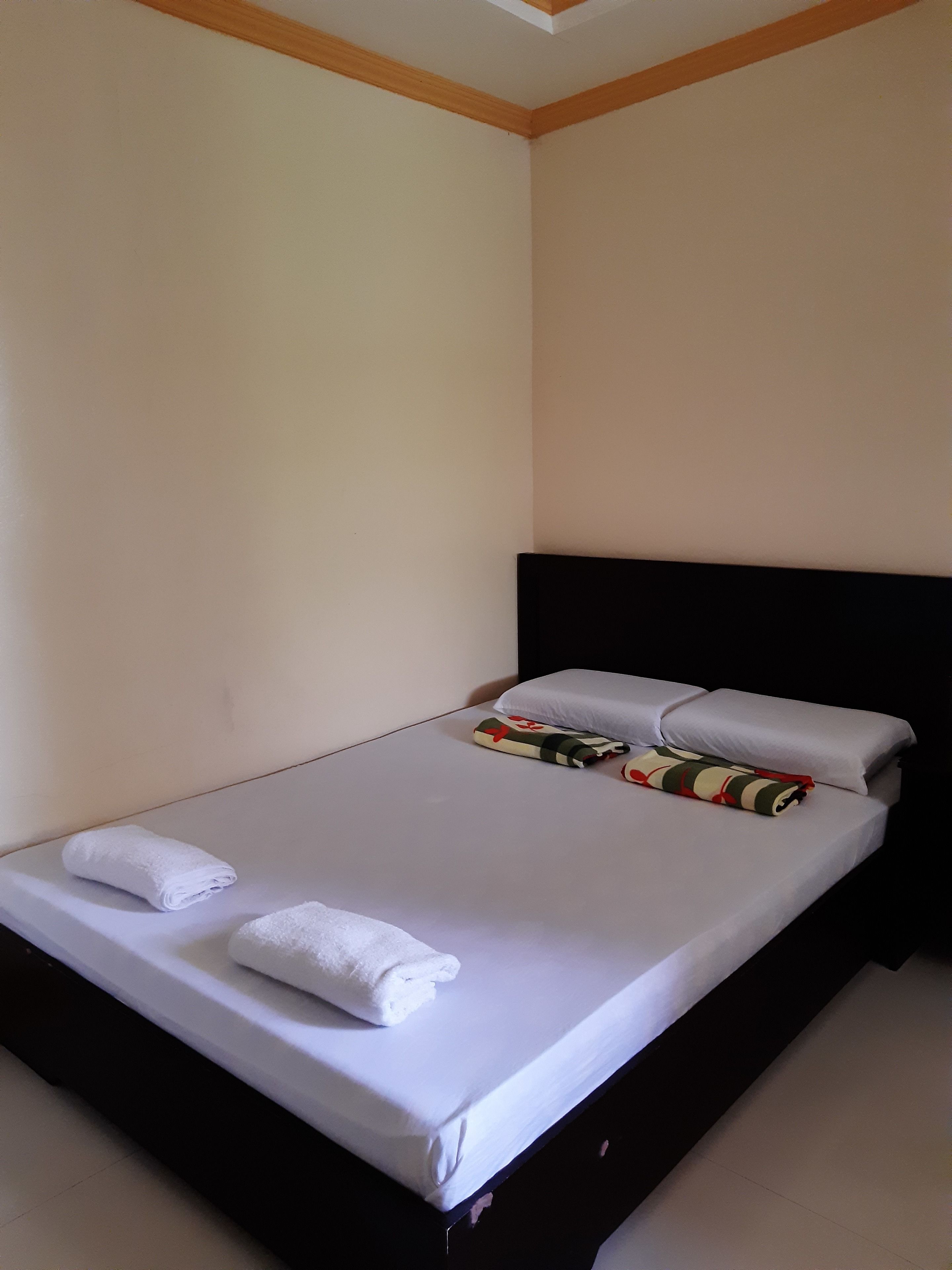 A single bed with white linens, two pillows, and two folded towels.