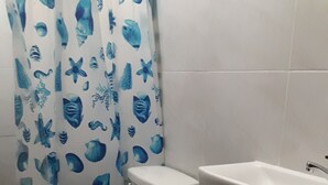 A bathroom with a toilet, a sink, and a blue trash bin. - Pabua's Cottages (Mambajao)