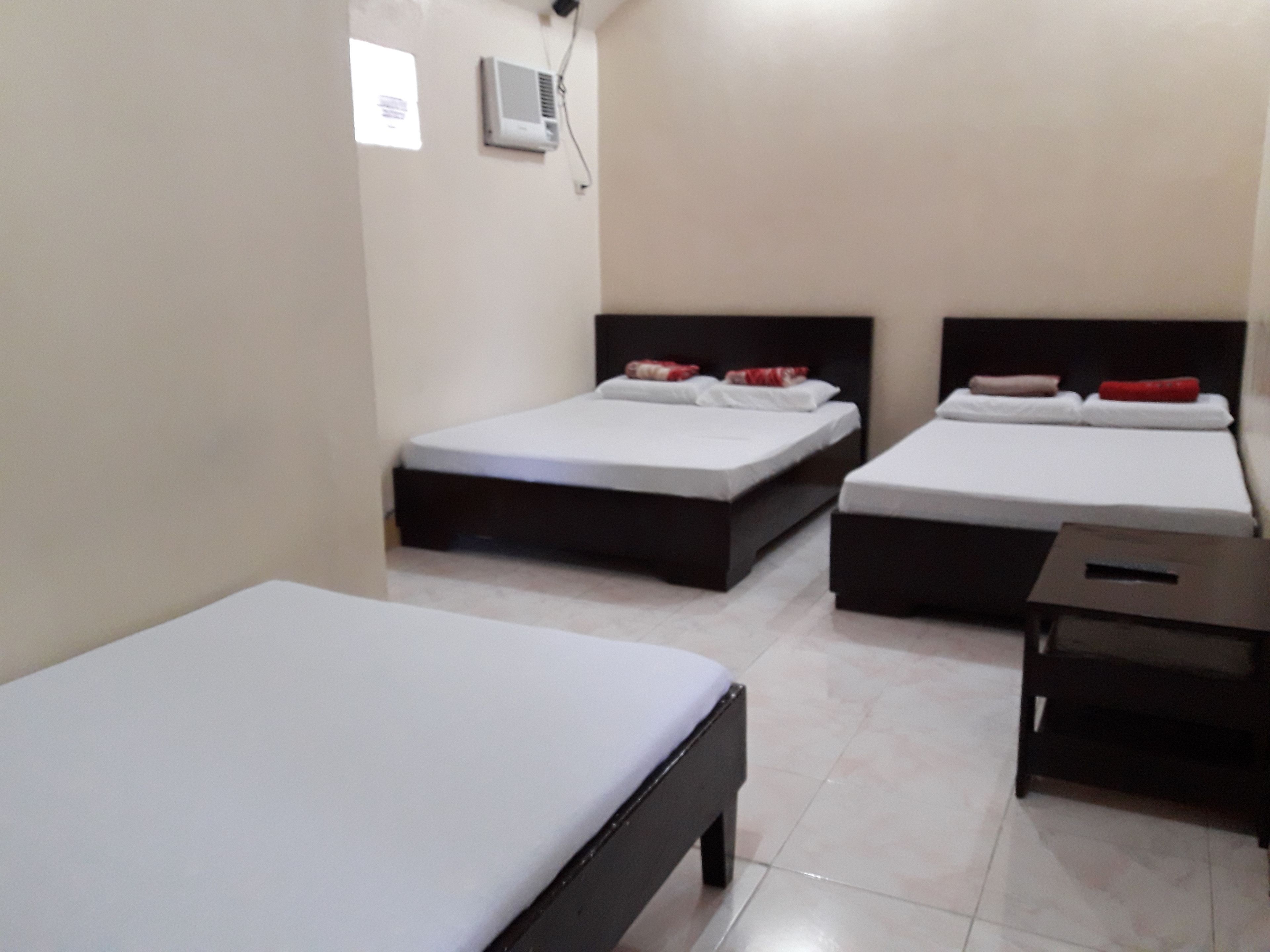 A hotel room with two single beds, a small table, and a wall-mounted air conditioner.
