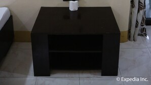 A television mounted on a wall, a remote control on a small table, and a power outlet. - Pabua's Cottages (Mambajao)