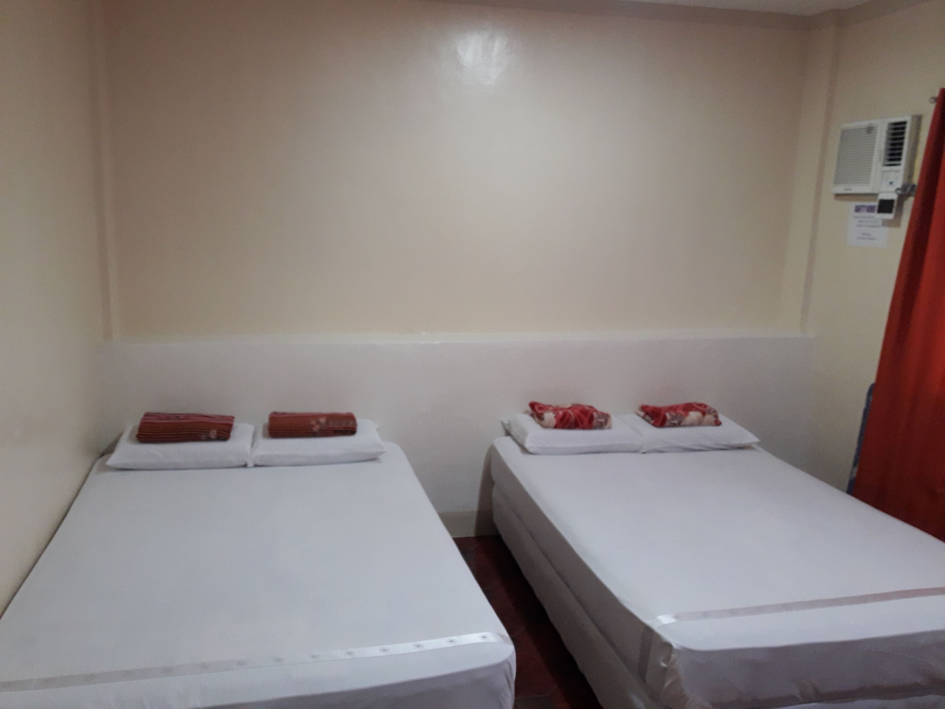 Una habitación de hotel pequeña y sencilla con dos camas, cada una con ropa blanca y almohadas rojas.