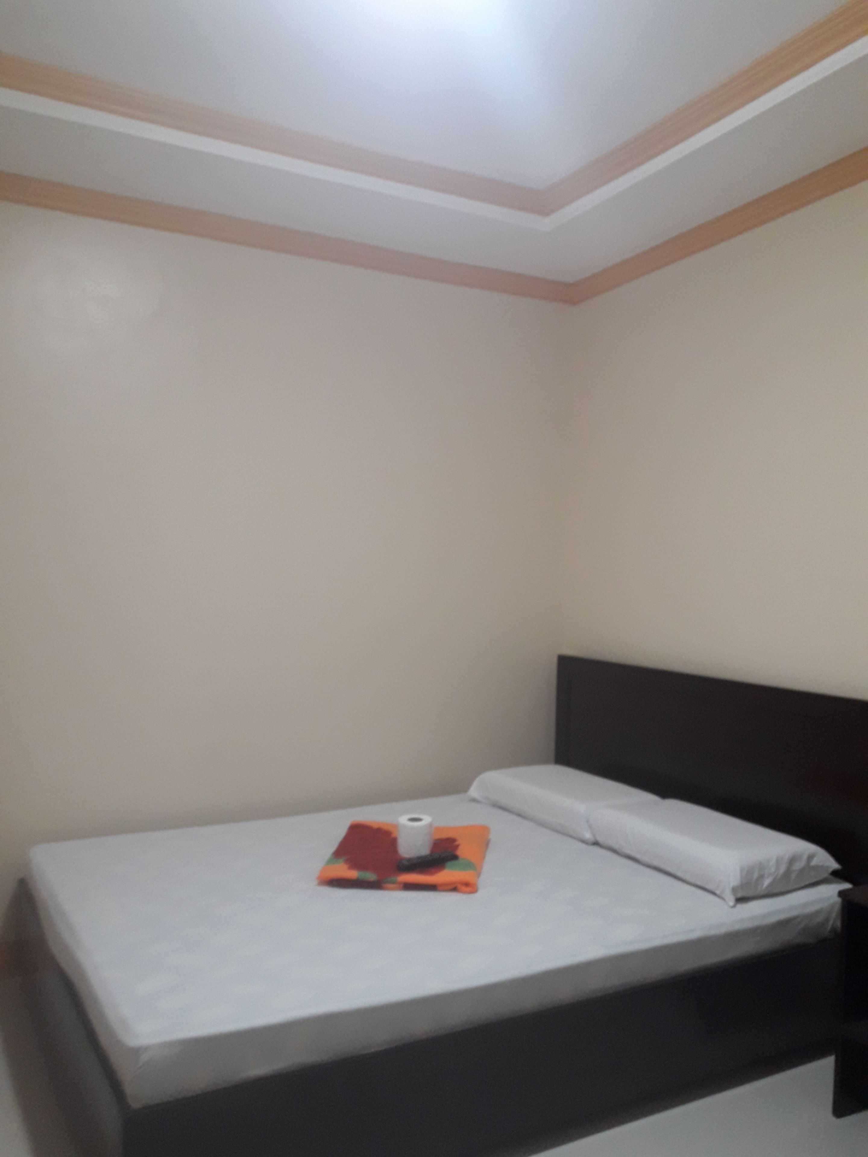 Una cama individual con colchón blanco y cabecera oscura en una habitación con paredes lisas y un diseño de techo sencillo.