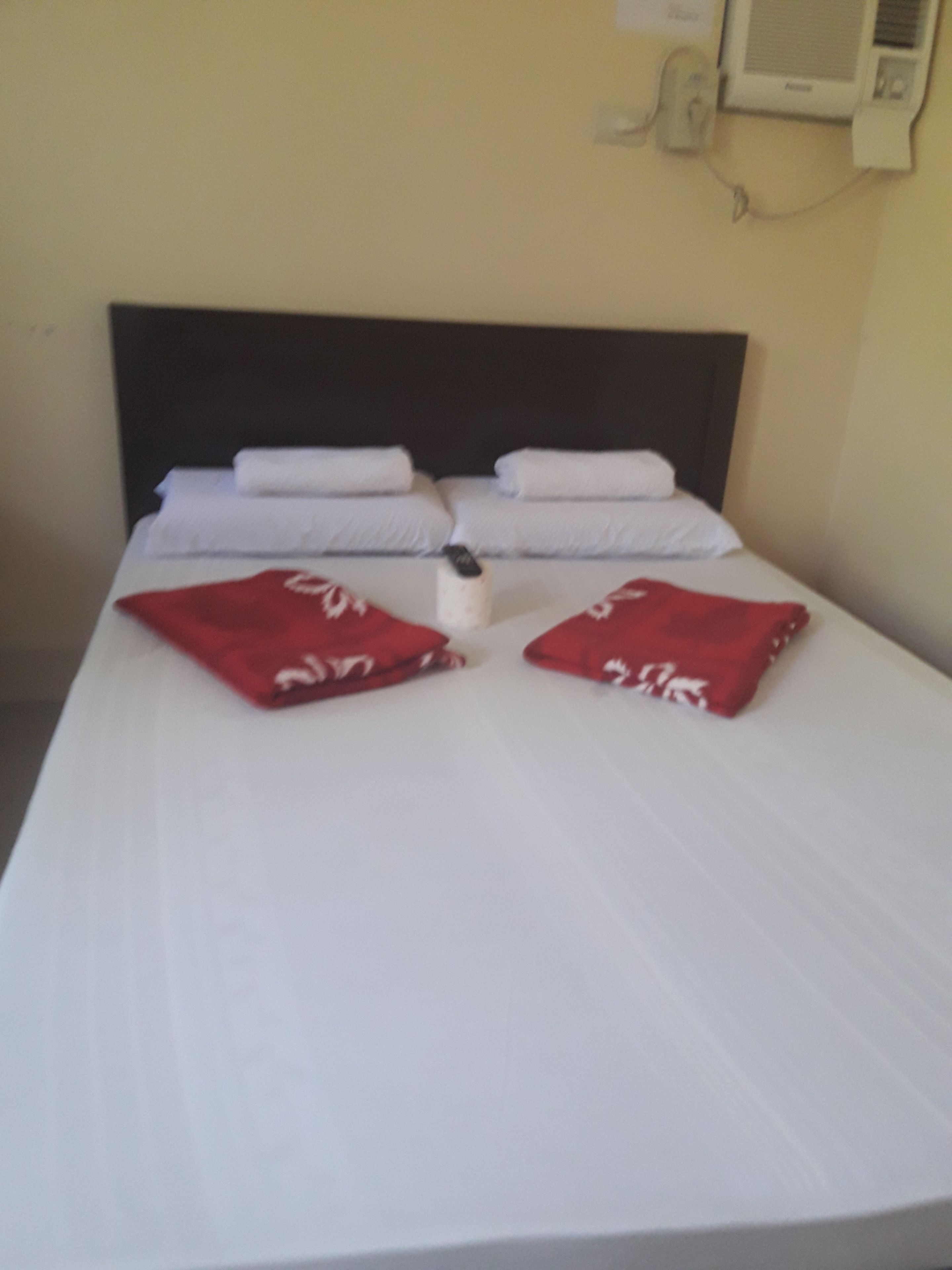 A neatly made bed with white linens and two red pillows.