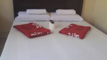 A neatly made bed with white linens and two red pillows.