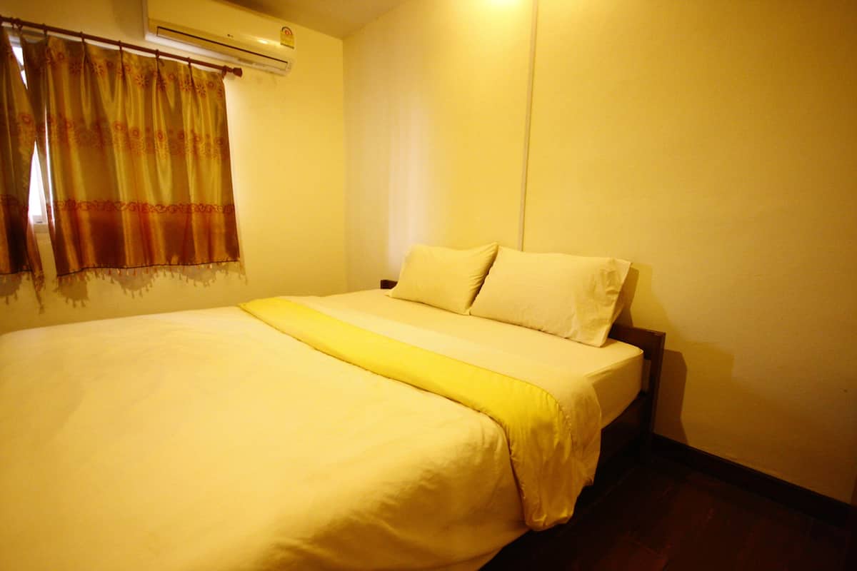 A hotel room with a bed, a window with curtains, and an air conditioning unit on the wall.