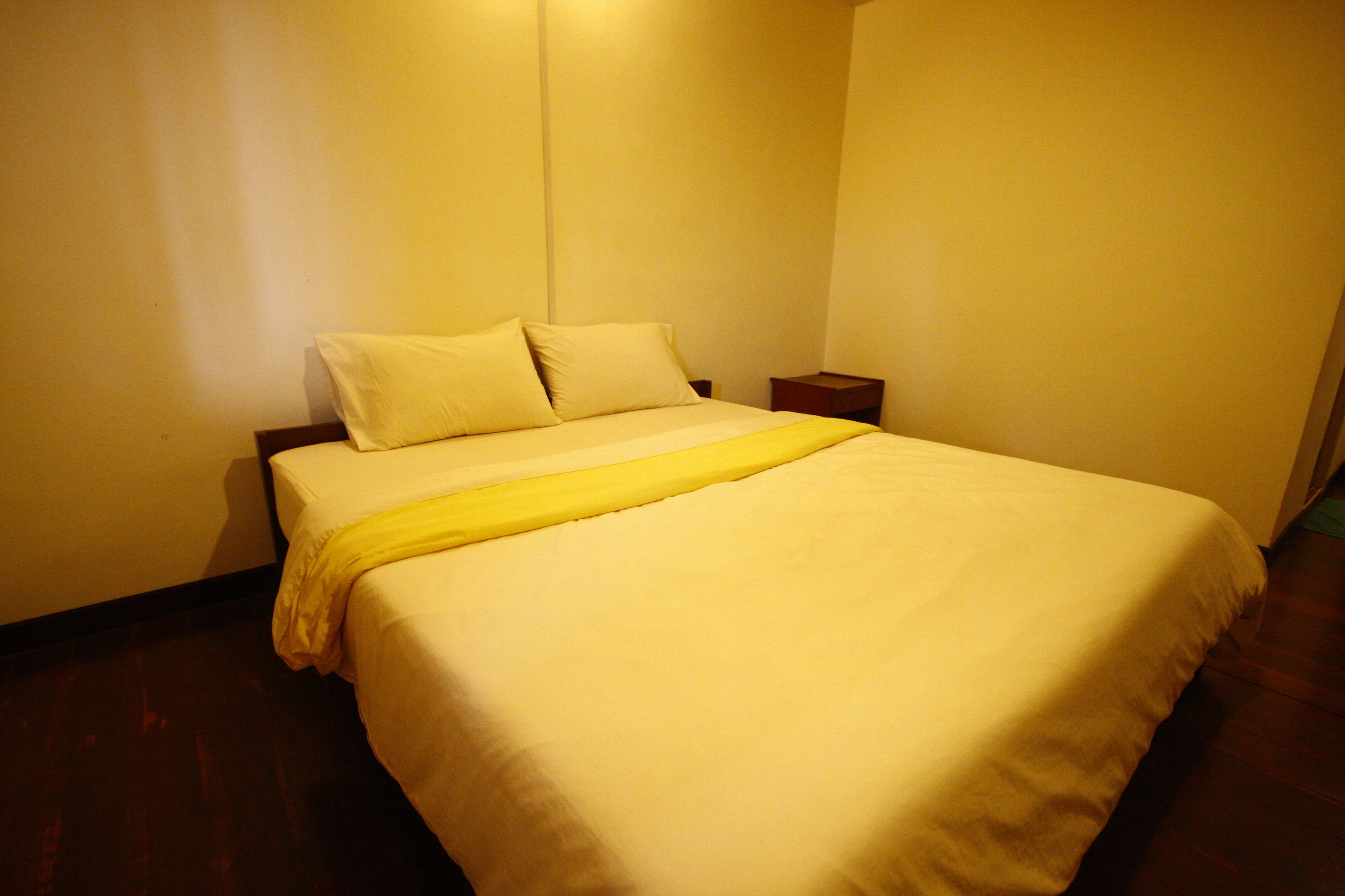 Una cama bien tendida con ropa blanca y un plaid amarillo.