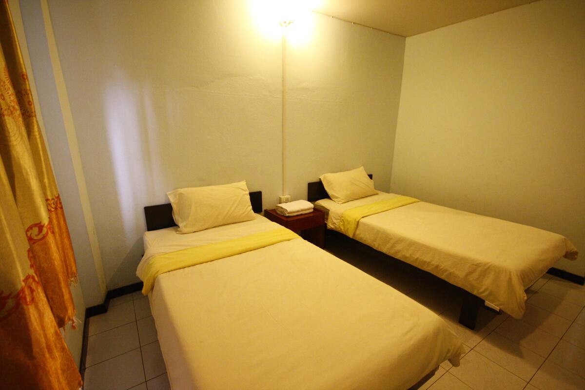 A room with two single beds, a bedside table with a lamp, and a curtain.
