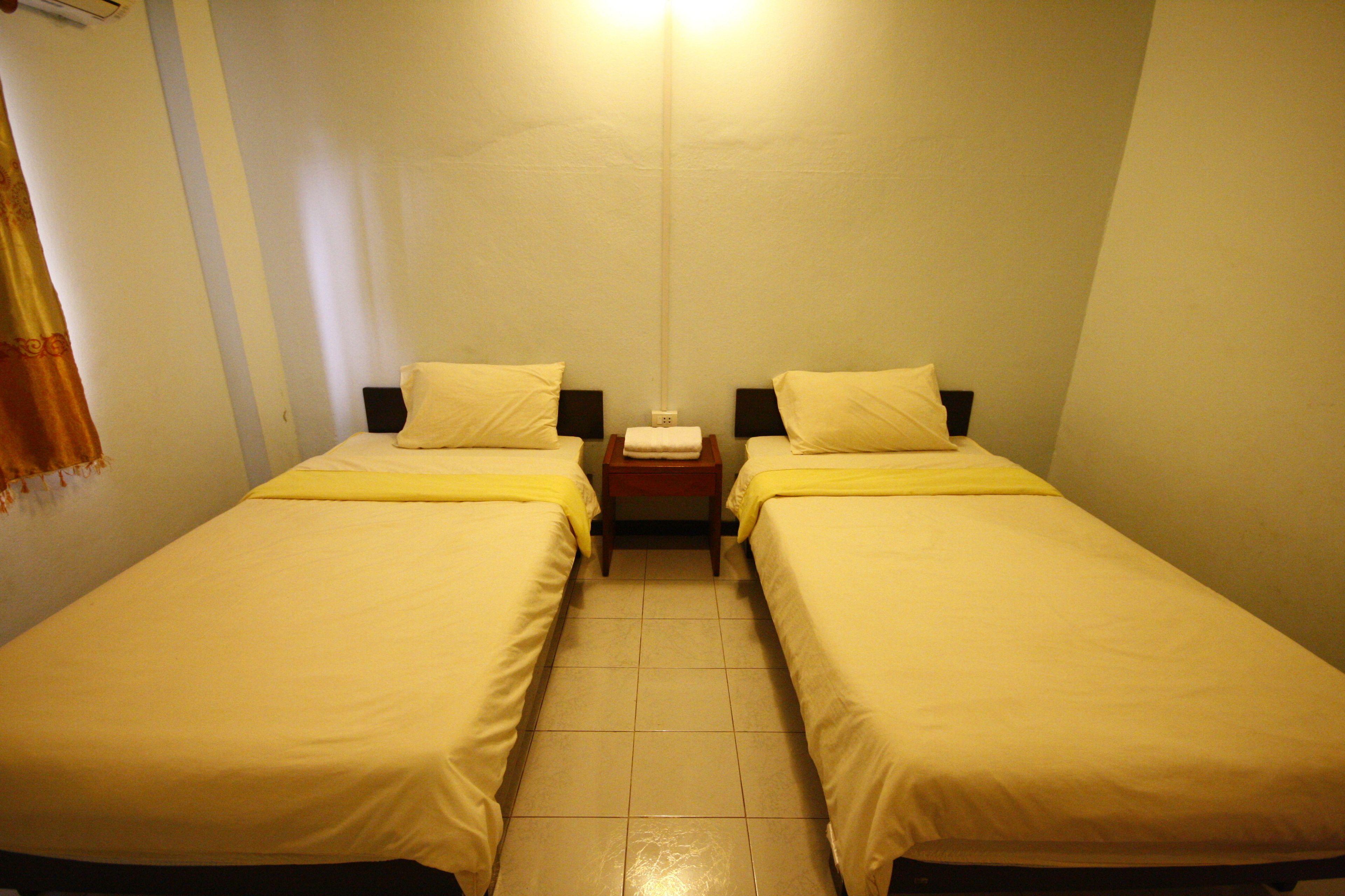 A small, clean room with two single beds, a nightstand, and a wall-mounted light.