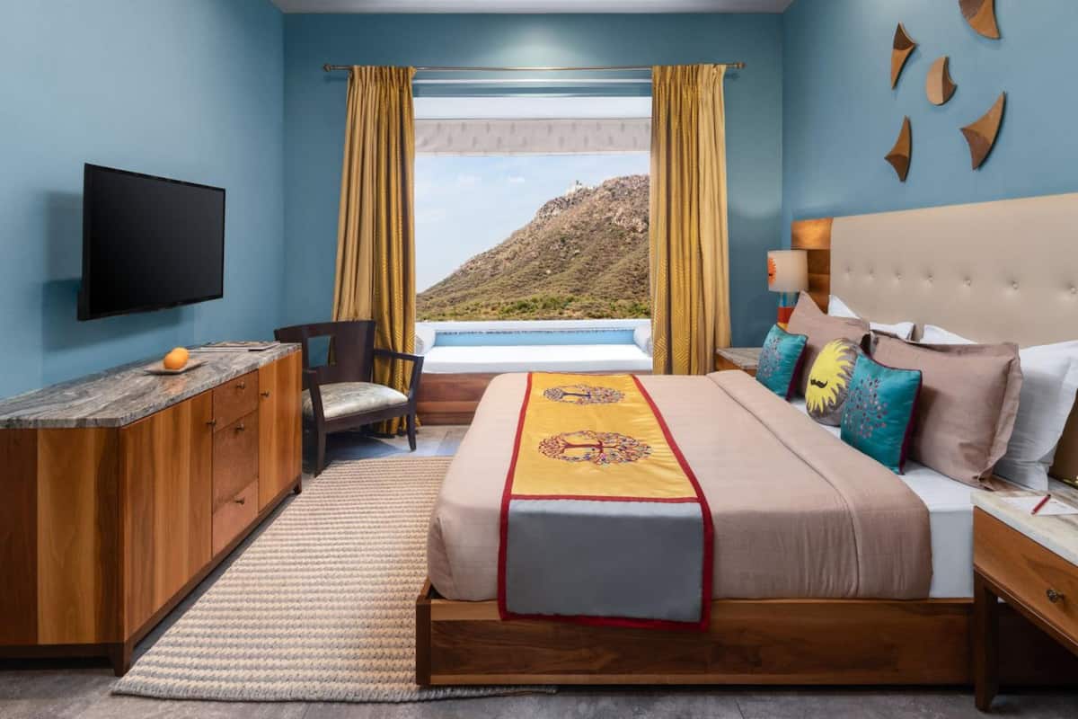 A bedroom with a bed, a TV, a desk, and a window with a view of a mountain.