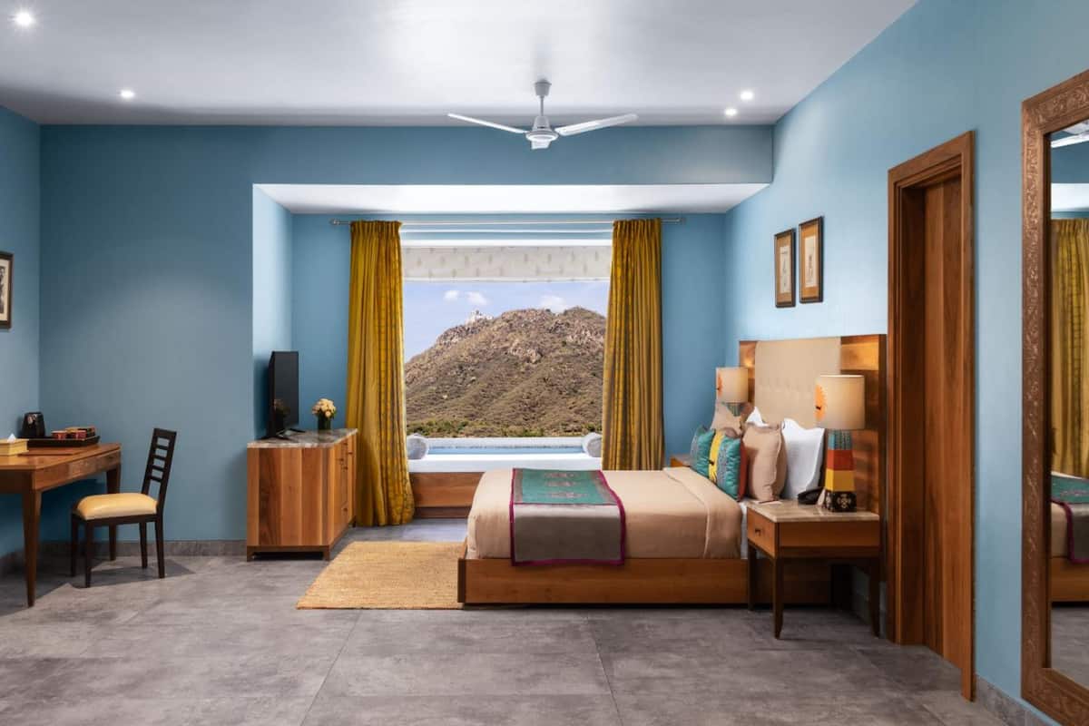 A bedroom with a bed, a desk, a chair, a TV, and a view of a mountain.