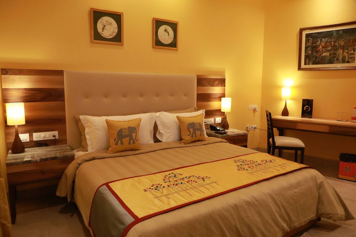 A hotel room with a large bed, two bedside tables, a desk, a chair, and wall-mounted clocks.