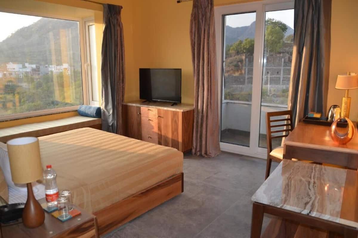 Une chambre dâhĂŽtel avec un lit, une tĂ©lĂ©vision, un bureau avec une lampe, une chaise et une vue sur lâextĂ©rieur.