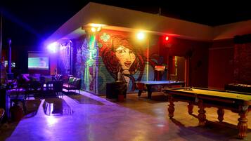 Una mesa de billar, una pantalla de proyector y un mural en una habitación con poca luz.