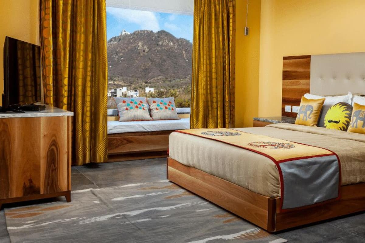 A hotel room with a bed, bedside tables, a TV, and a view of mountains.