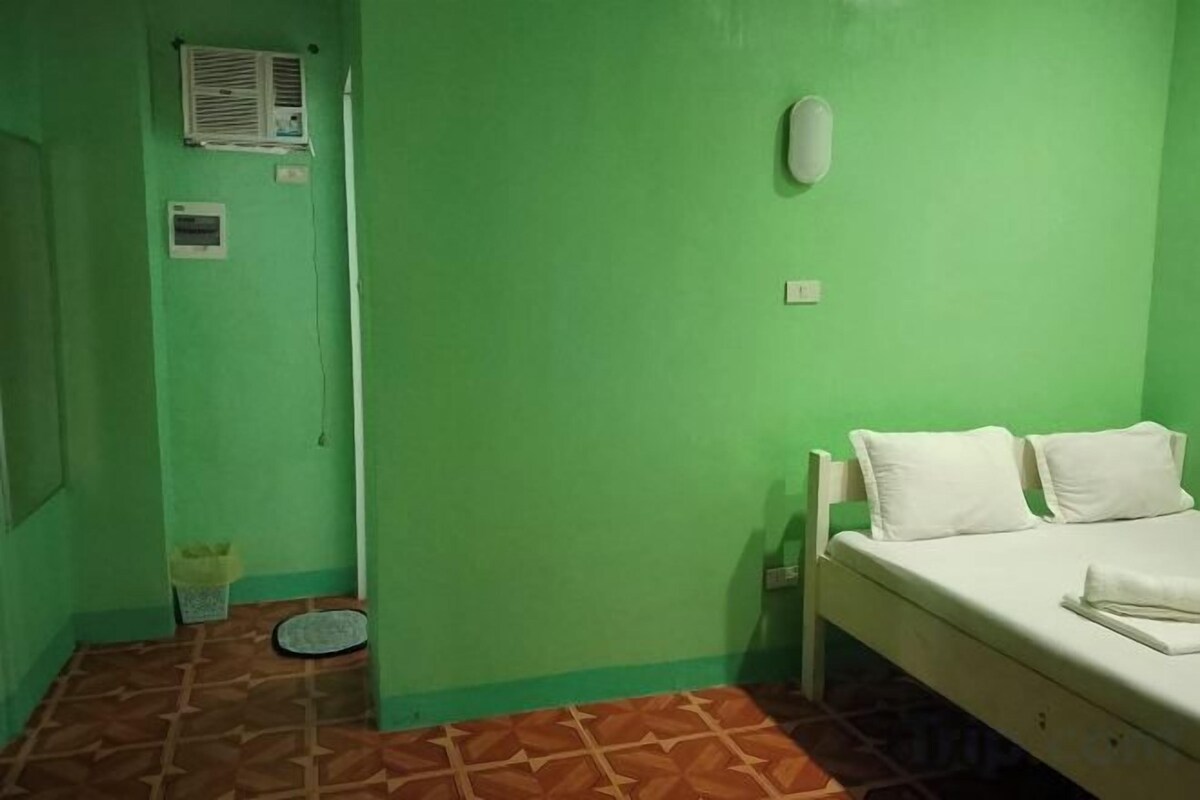 Una habitación con una cama individual, una mesita de noche pequeña, una lámpara de pared y una ventana.