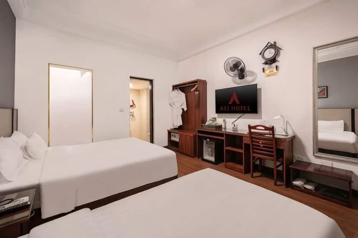 A hotel room with two beds, a desk with a chair, a TV, a wardrobe, and a mirror.
