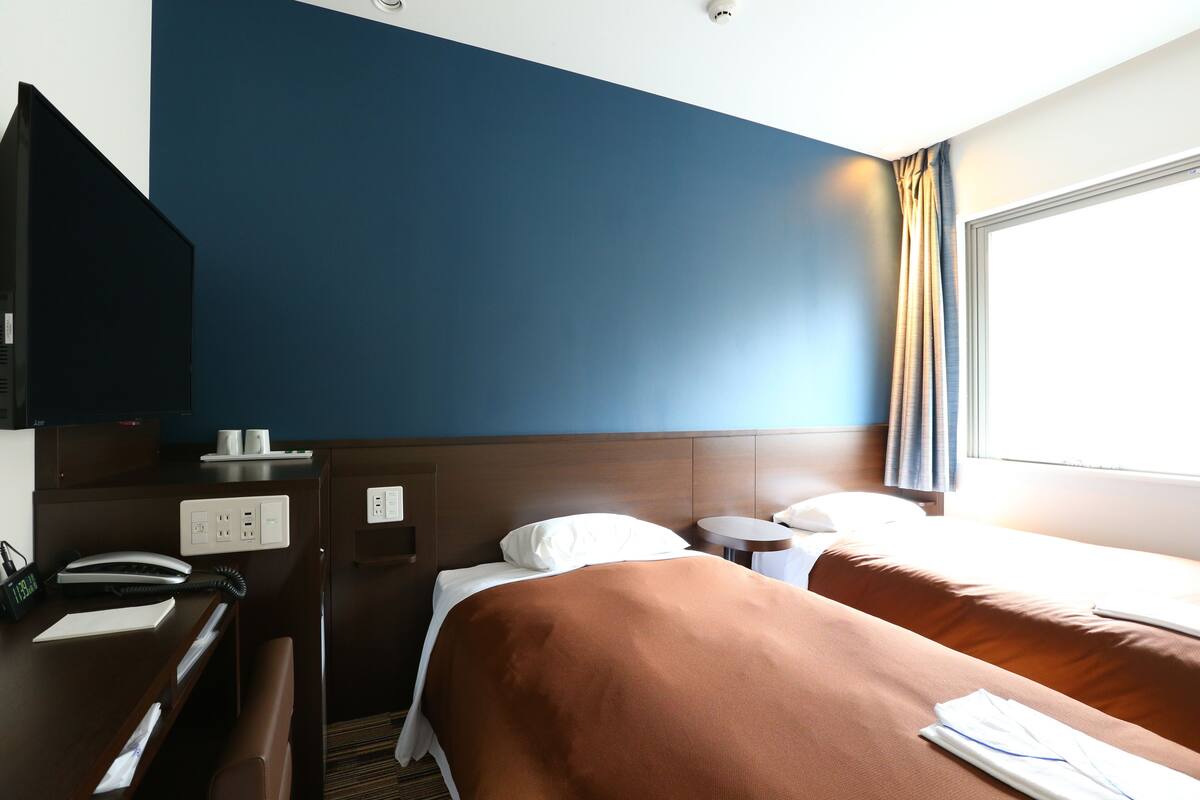 A hotel room with a bed, bedside tables, a desk with a telephone, and a television.