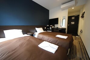 Ein Hotelzimmer mit zwei Betten, einem Schreibtisch, einem Stuhl, einem kleinen runden Tisch, einem Spiegel und einer Klimaanlage.
