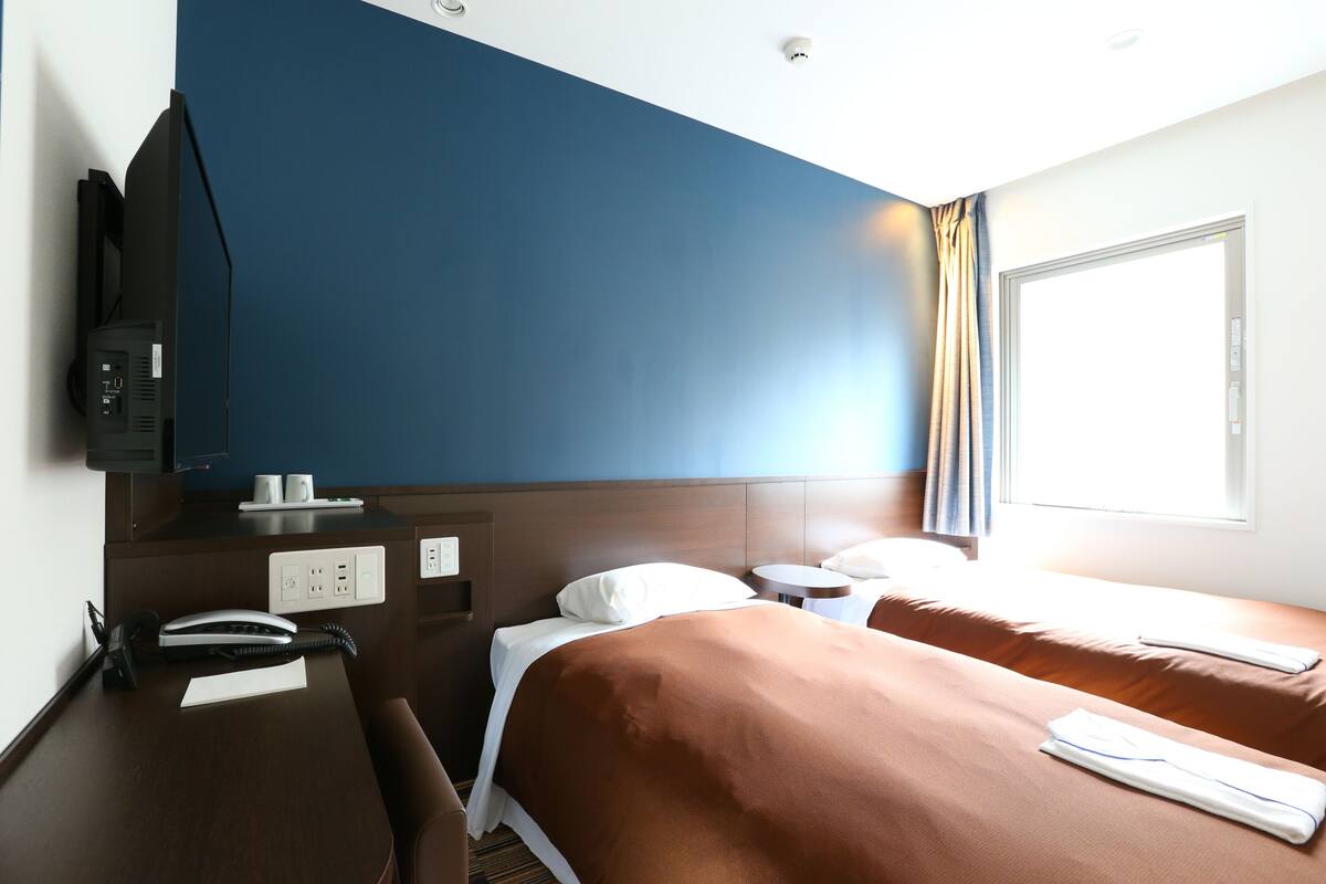 A hotel room with a desk, two beds, a TV, and a window with curtains.