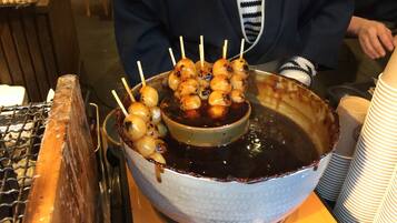 A bowl of skewered food with a dark sauce, placed on a table with a metal rack and stacked paper cups.