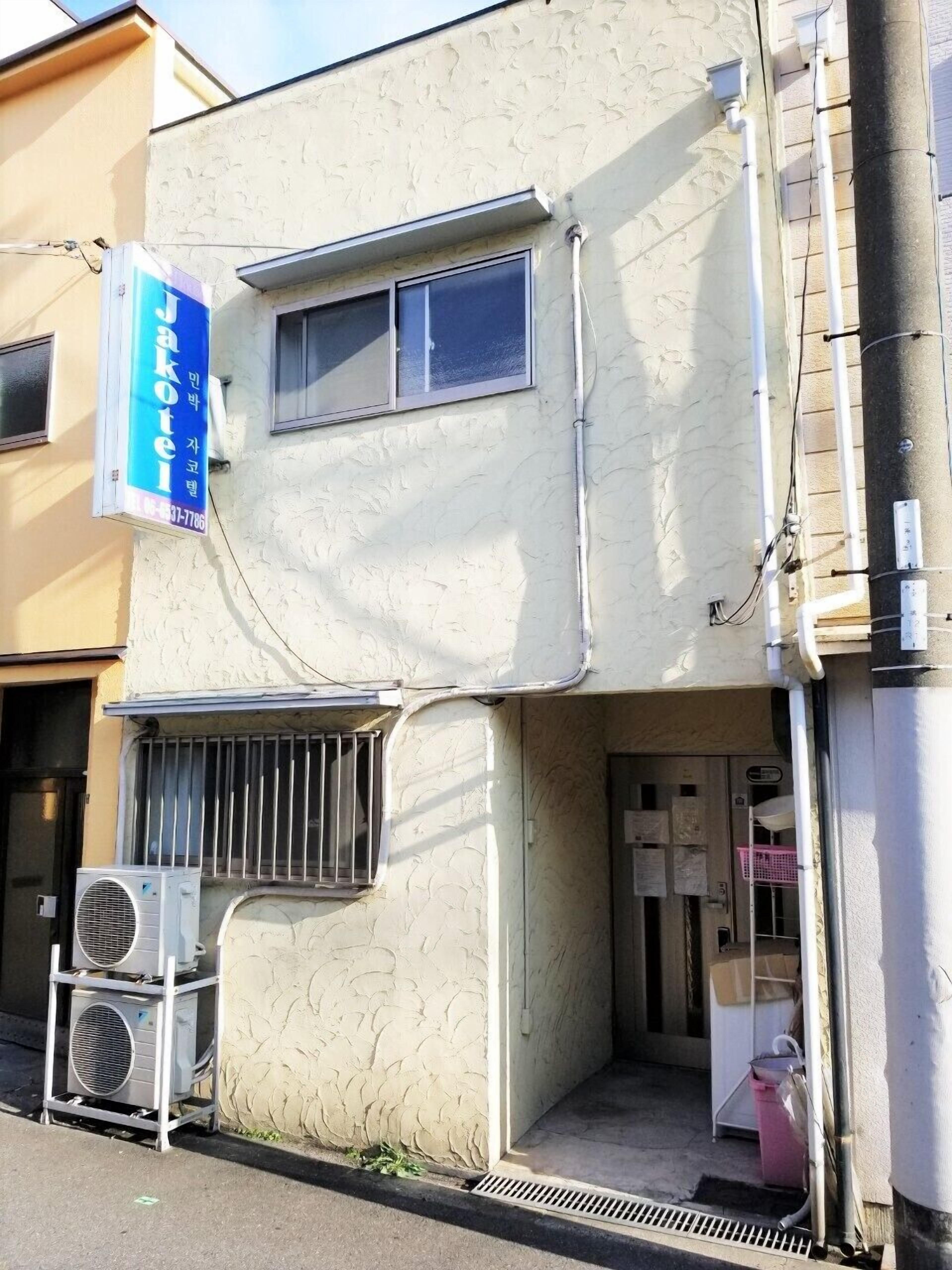 A building with a beige exterior, a blue sign on the left, and a window with a metal grill.