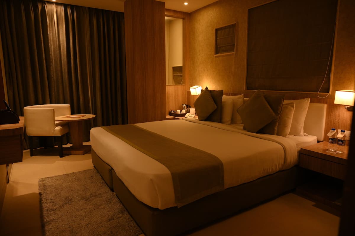 A hotel room with a large bed, a desk, a chair, a nightstand with a lamp, and a mirror.
