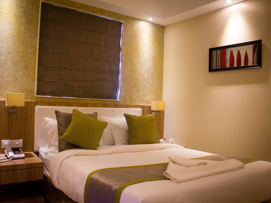 A hotel room with a bed, bedside lamps, a nightstand, a window with blinds, and a framed picture on the wall.
