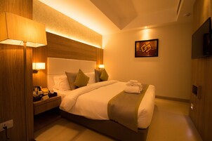A hotel room with a large bed, bedside lamps, a flat-screen TV, and a painting on the wall.