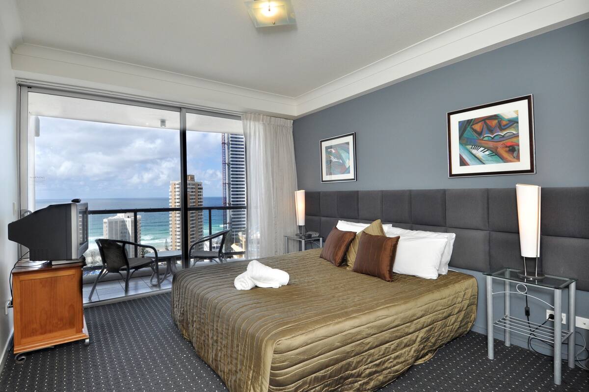 Une chambre d’hôtel avec un grand lit, une télévision, un bureau et un balcon offrant une vue sur la ville.