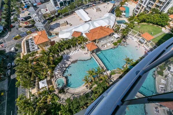 An aerial view of a resort with multiple swimming pools, palm trees, and a large building with a distinctive roof.