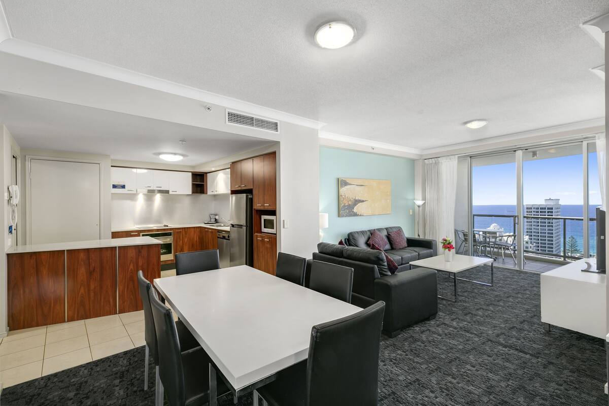 Une chambre d’hôtel moderne dotée d’un coin repas, d’un canapé, d’un balcon avec vue sur la ville et d’une cuisine.