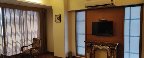 Une pièce avec une chaise en bois, une cheminée, un téléviseur fixé au mur et une fenêtre avec des rideaux.