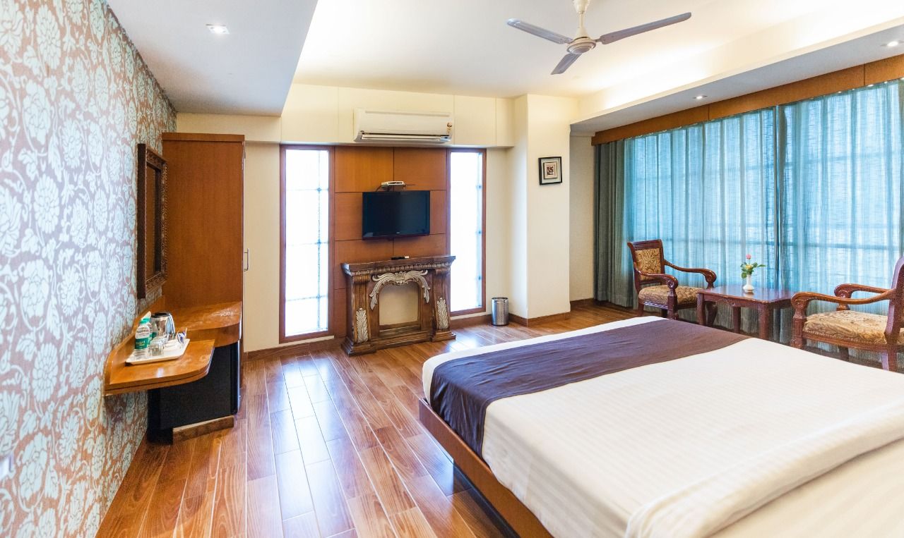 Habitación de hotel con cama, escritorio, televisor y ventana con cortinas.